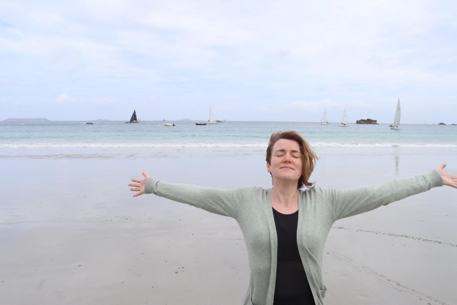 Nicole steht mit weit ausgebreiteten Armen am Strand vor dem Meer