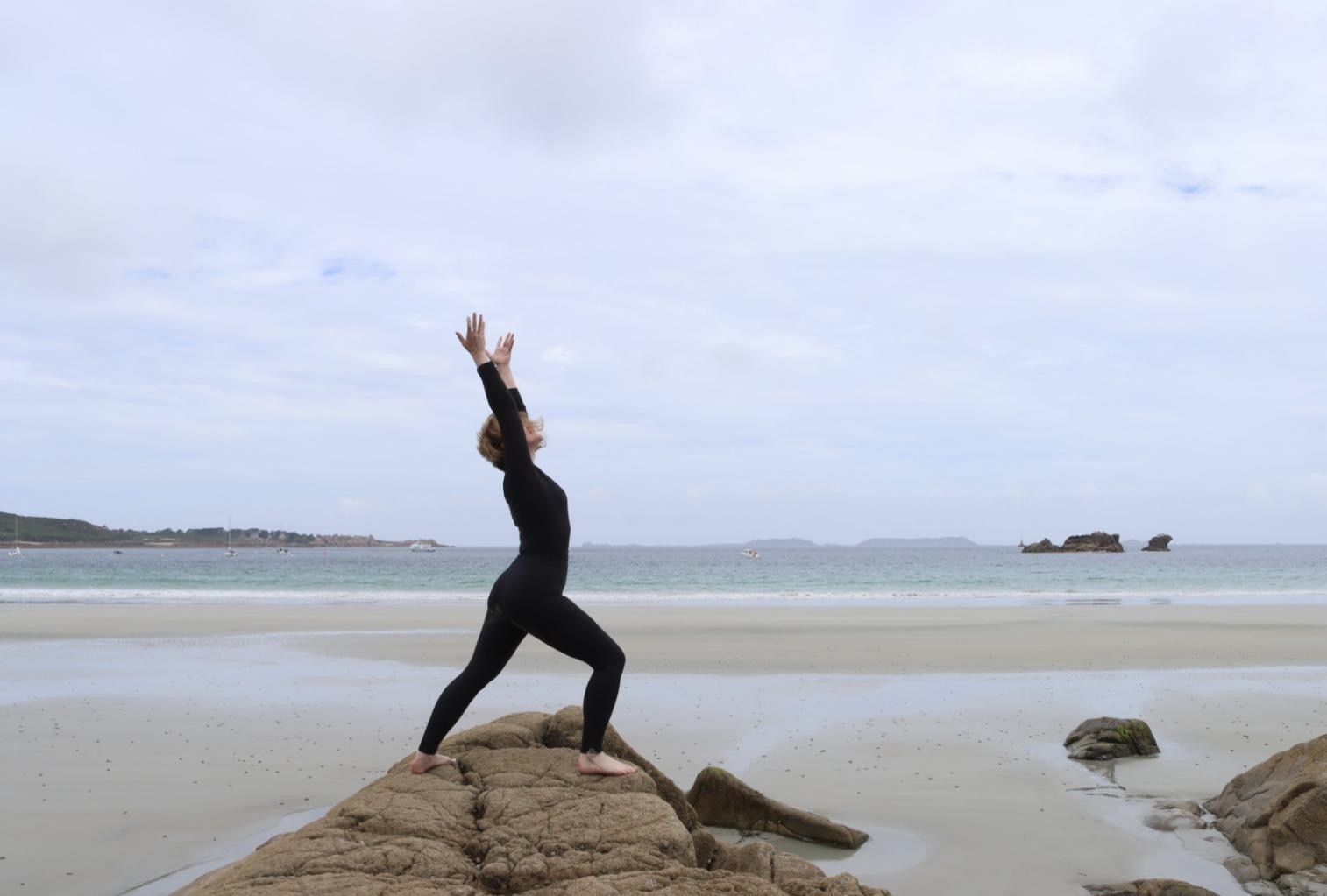 Nicole in einer Yoga-Haltung mit gestreckten Armen auf einem Felsen am Meer